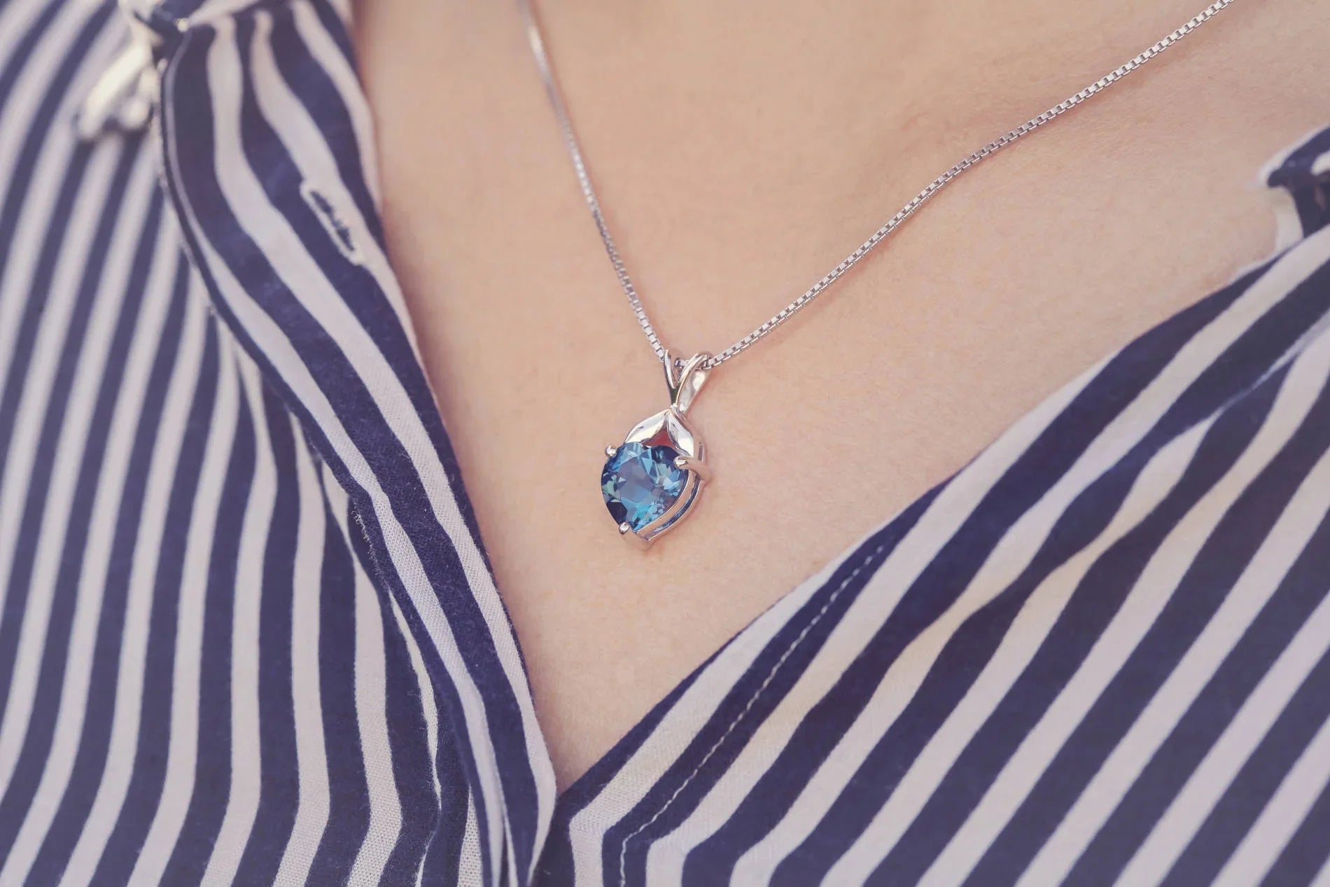 Necklace with a blue gemstone pendant worn by a person in a striped outfit
