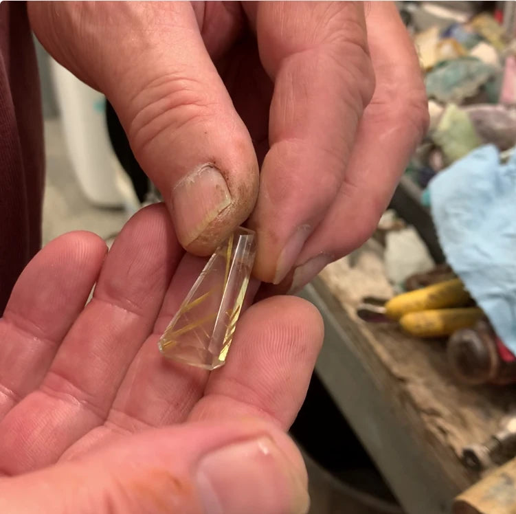 Person holding a clear crystal or gemstone between their fingers with a blurred background.
