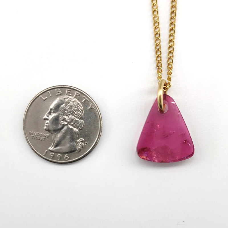Pink tourmaline pendant on a gold-filled  chain next to a quarter for scale on a white background