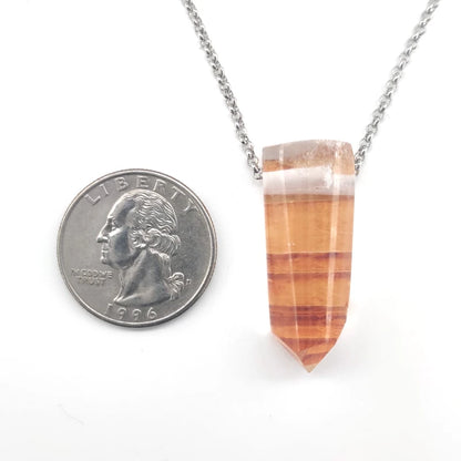 Necklace with a tangerine quartz pendant next to a quarter for scale on a white background