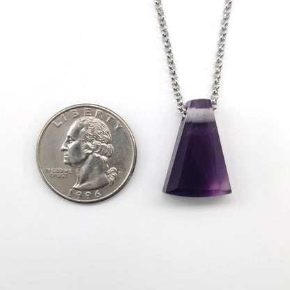 Amethyst pendant on a chain next to a quarter for scale on a white background