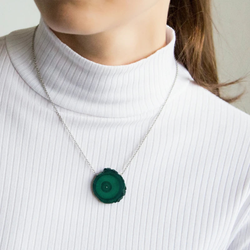 Person wearing a necklace with a malachite pendant on a plain background