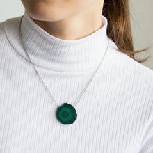 Person wearing a necklace with a malachite pendant on a plain background