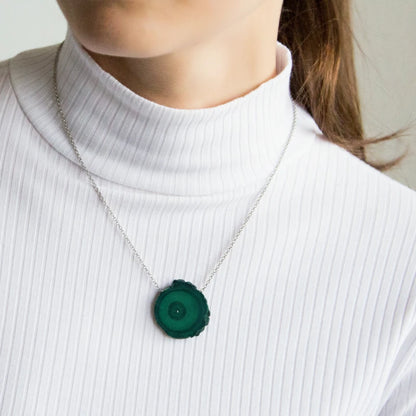 Person wearing a necklace with a malachite pendant on a plain background