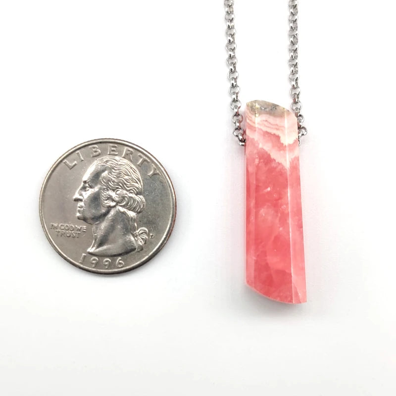 Rhodochrosite pendant necklace next to a quarter for size comparison on a white background