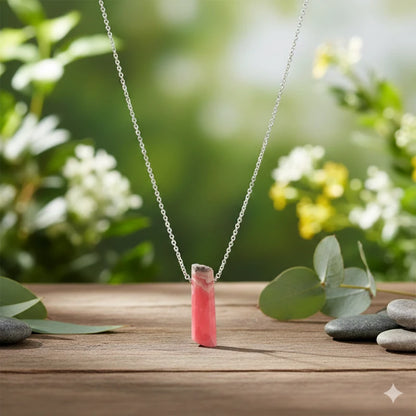 Necklace with a rhodochrosite pendant on a wooden surface with greenery in the background