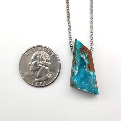 Chrysocolla pendant on a chain next to a quarter for scale on a white background