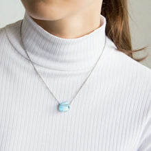 Close-up of a woman wearing a necklace with a blue topaz pendant