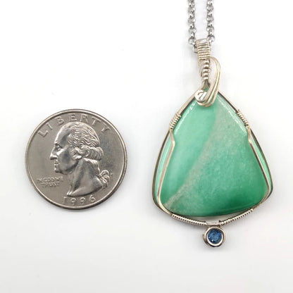 Green pendant with silver wire wrapping next to a quarter on a white background