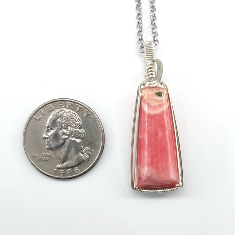 Wire-wrapped rhodochrosite pendant on a chain next to a quarter for scale on a white background