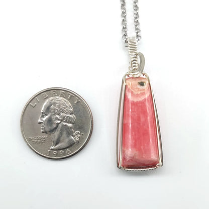 Wire-wrapped rhodochrosite pendant on a chain next to a quarter for scale on a white background