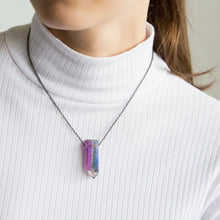 Close-up of a woman wearing the neckless with a Angel Aura Quartz pendant featuring a polished crystal point treated to reveal a shimmering display of iridescent colors, shifting between soft purples, blues, and hints of gold.