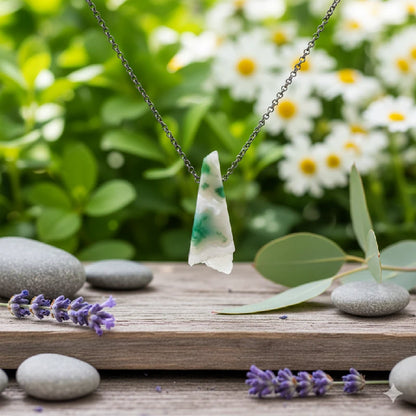 Necklace with a white agate pendant on a wooden surface with stones and lavender flowers, blurred greenery in the background