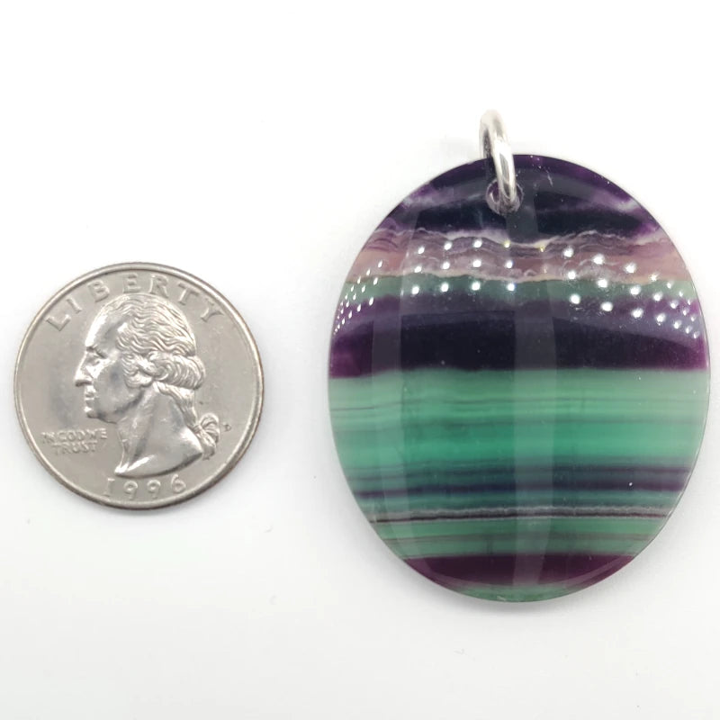 Fluorite pendant next to a quarter for size comparison on a white background