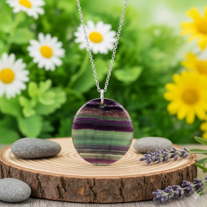 Necklace with a fluorite pendant on a wooden stand with flowers in the background