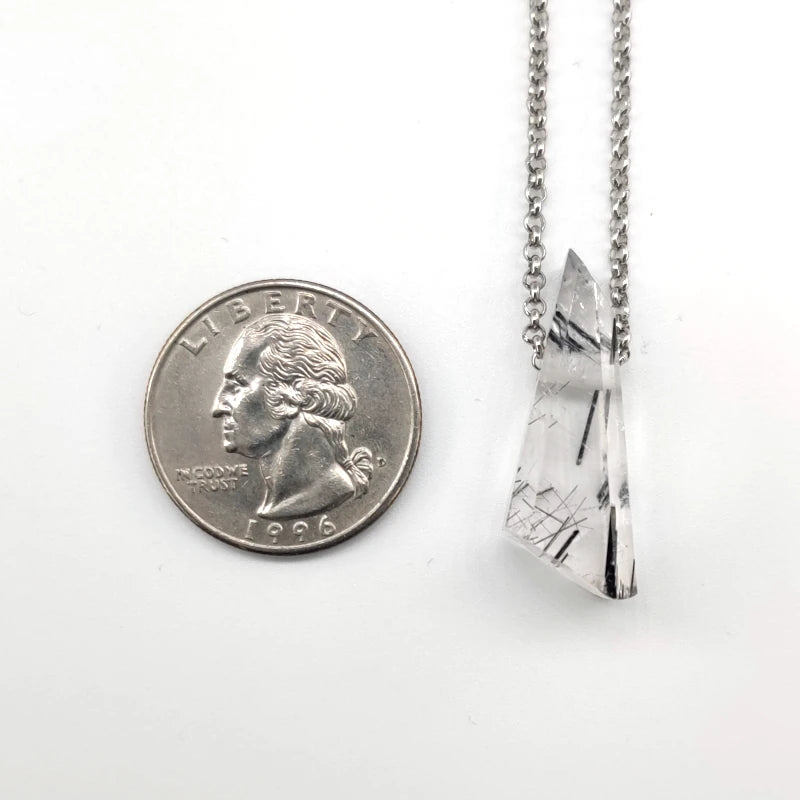 Crystal pendant on a chain next to a quarter for scale on a white background