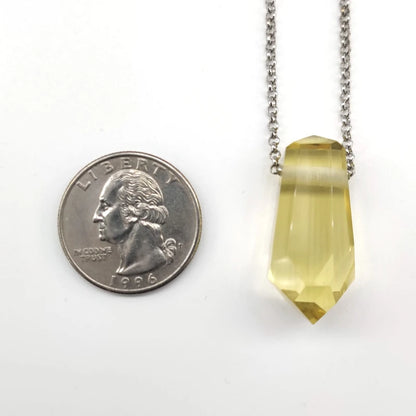 Yellow crystal pendant on a chain next to a U.S. quarter for size comparison on a white background