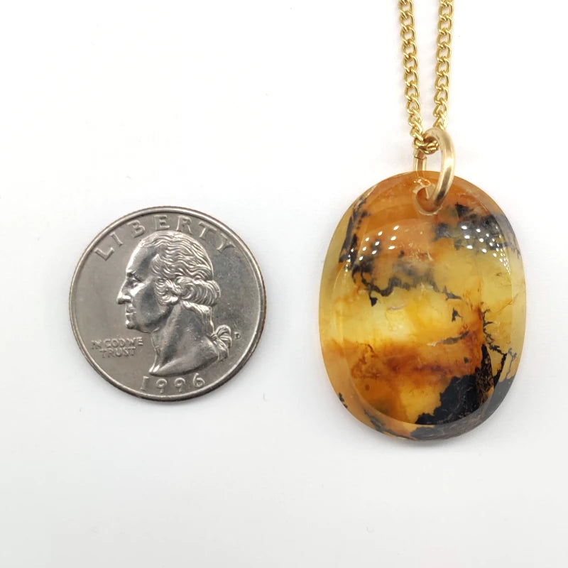 Marbled pendant on a gold filled chain next to a quarter for size comparison on a white background