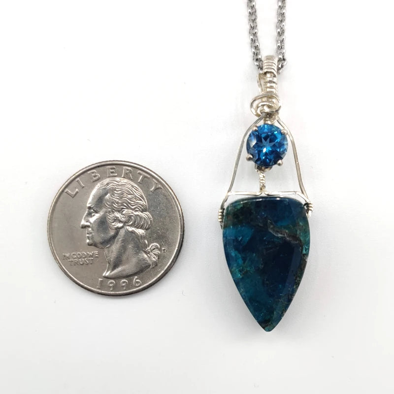 Blue pendant necklace with a blue gemstone next to a U.S. quarter for scale on a white background