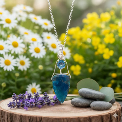 Blue pendant necklace on a wooden stump with flowers and stones in the background