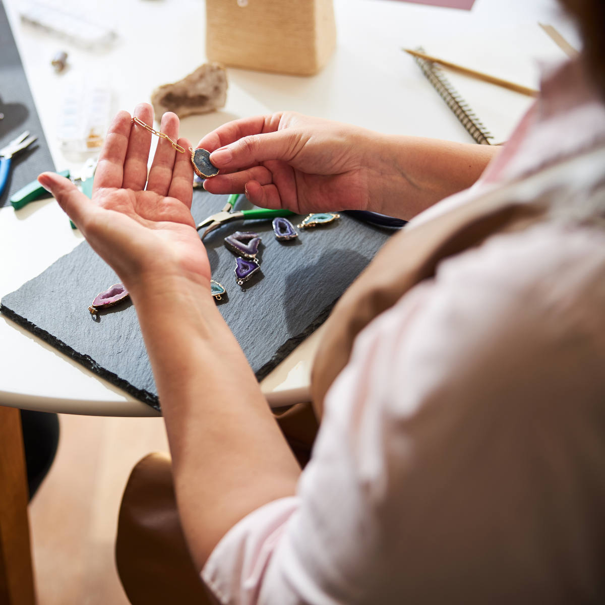 hands examining a gemstone pendant on a table with other gemstones