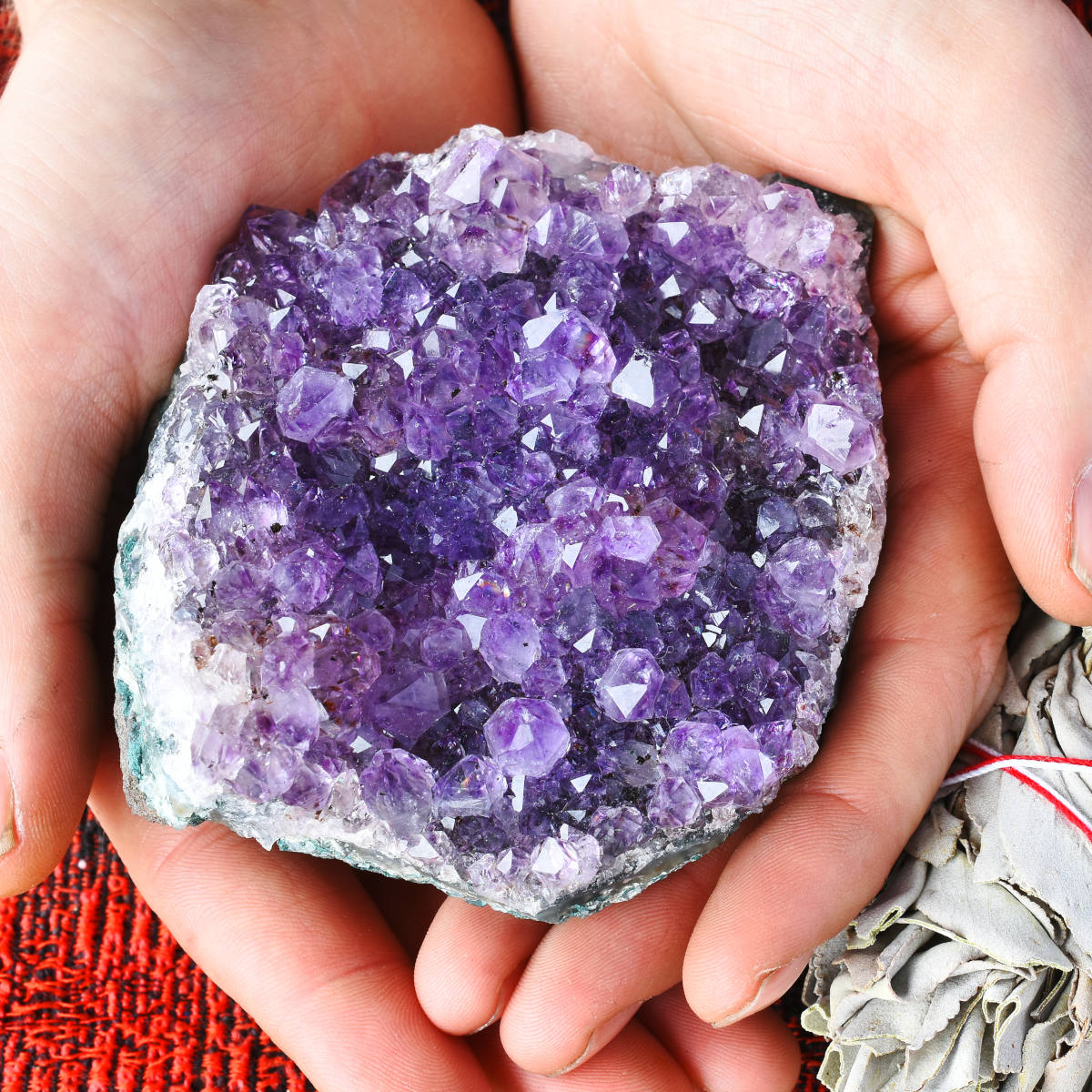 A pair of hands holding an amethyst geode